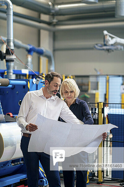 Businessman with colleague discussing over blueprint in industry