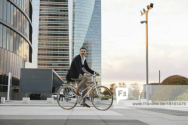 Mature commuter riding bicycle in front of office building at sunset