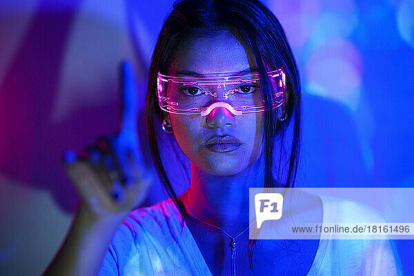 Young woman wearing futuristic glasses gesturing with finger