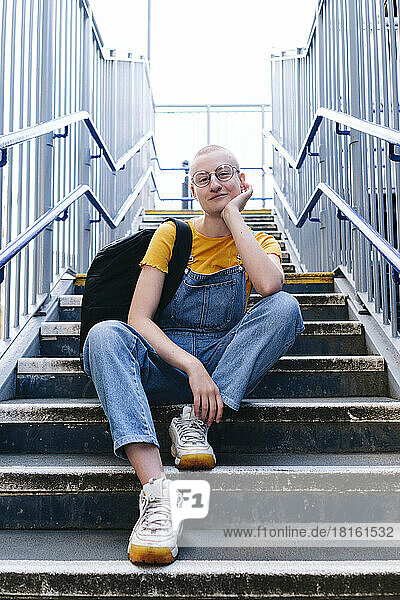 Androgynous person with backpack sitting on staircase