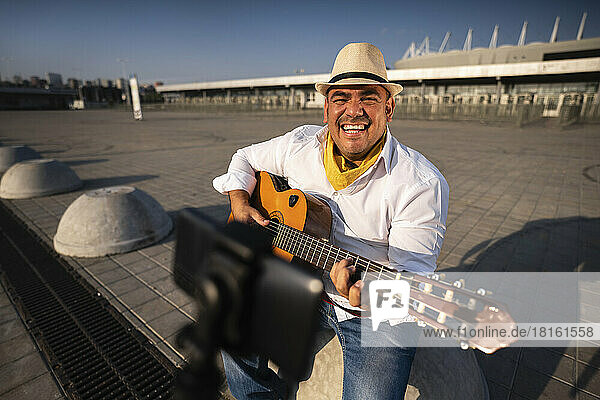 Smiling guitarist playing guitar in front of mobile phone on tripod