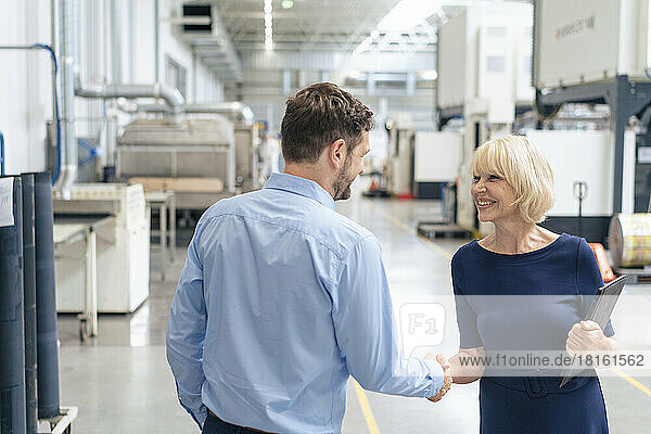 Smiling senior businesswoman holding laptop shaking hand with businessman