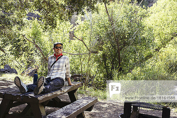 Happy man wearing sunglasses on wooden table in forest