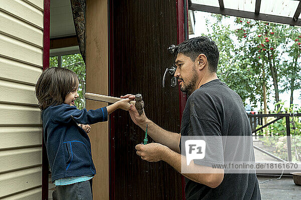 Smiling boy giving hammer to father at doorway
