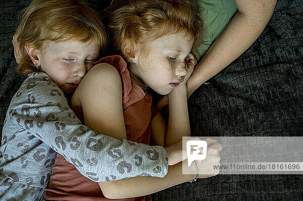 Liebevolle Geschwister umarmen sich und schlafen auf dem Schoß der Mutter