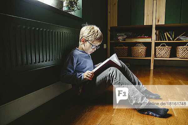 Boy reading book sitting on floor at home