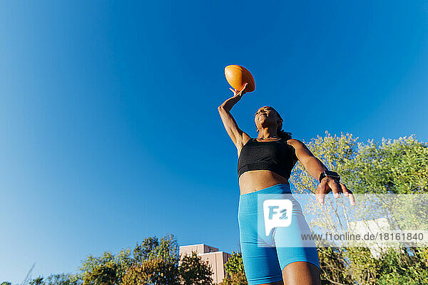 Young sports player throwing American ball on sunny day