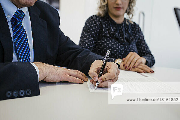 Mature businessman doing signature on document at desk