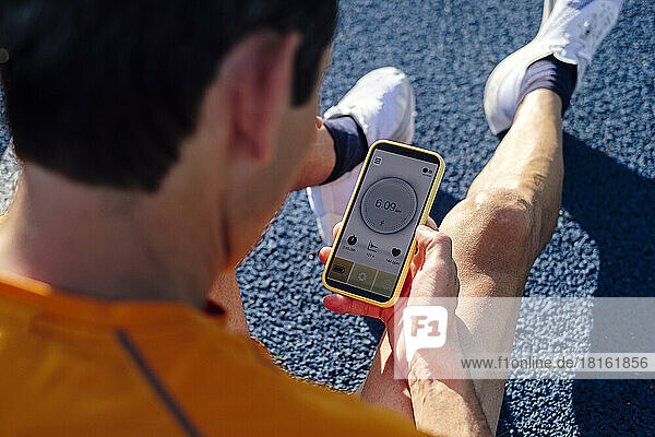Sportler mit Mobiltelefon sitzt auf der Strecke