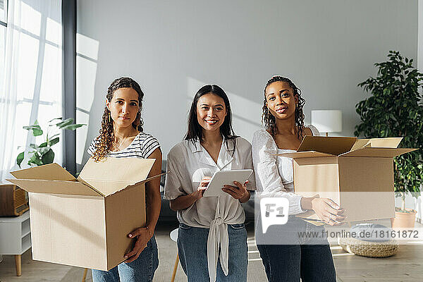 Smiling woman with tablet PC amidst friends carrying boxes at new home