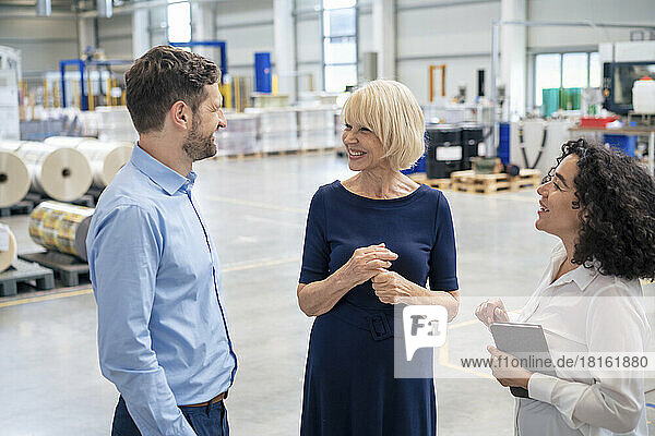 Smiling businesswoman holding tablet PC talking with colleagues in industry