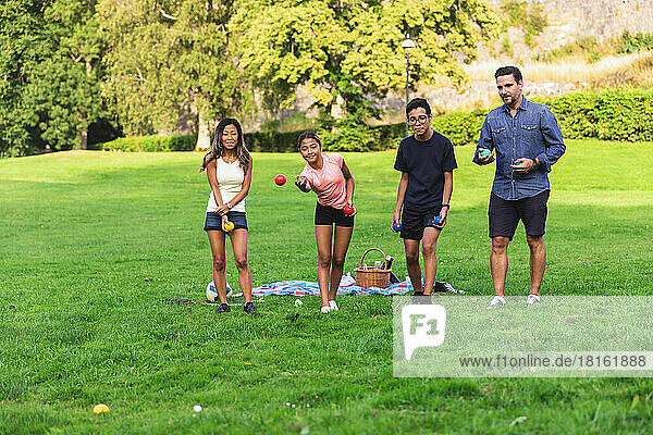 Multiracial family playing boules standing on grass in lawn
