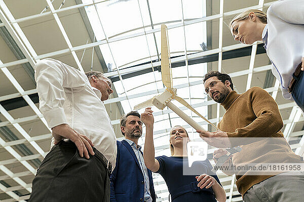 Smiling businesswoman with colleagues discussing over wind turbine model at industry