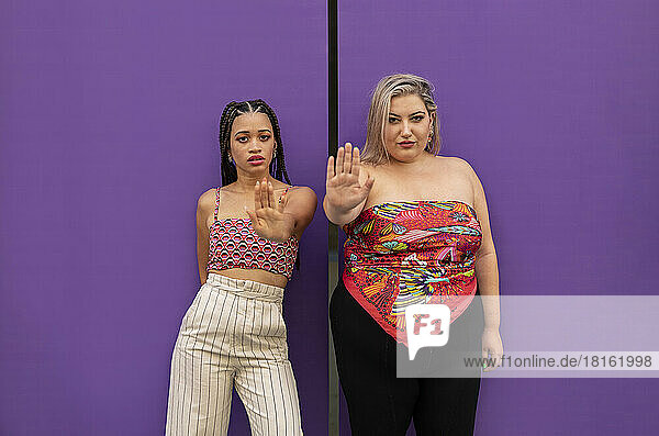 Young woman with friend gesturing stop sign in front of purple wall