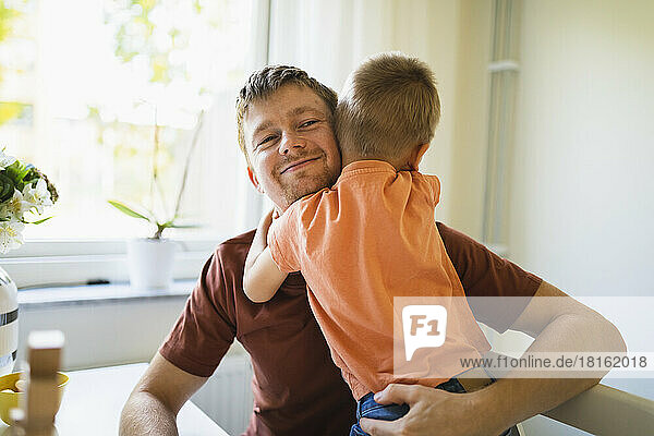 Junge umarmt lächelnden Vater zu Hause