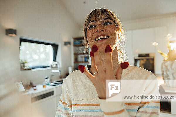 Happy woman with raspberries on fingers at home