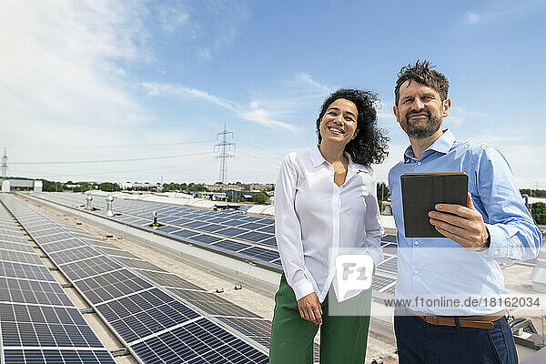 Smiling businessman holding tablet PC standing by businesswoman in front of solar panels