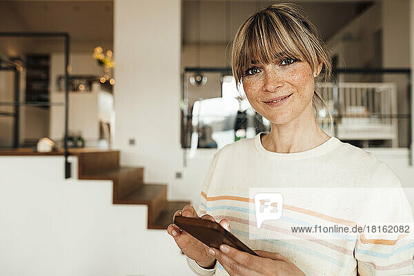 Smiling woman with bangs holding mobile phone at home