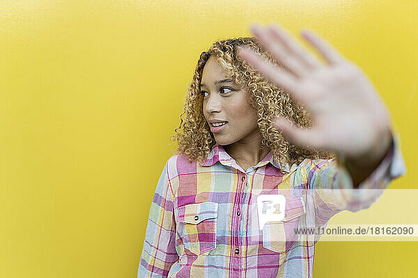 Young woman gesturing stop over yellow background