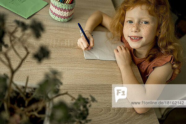 Lächelndes rothaariges Mädchen  das zu Hause mit Farbstift zeichnet