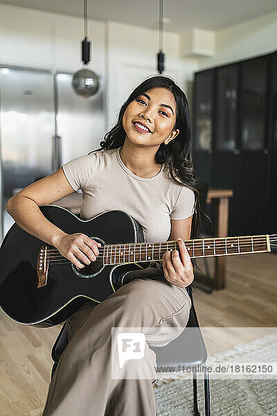 Smiling woman playing guitar at home