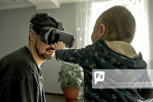 Baby boy looking at father wearing virtual reality simulator at home