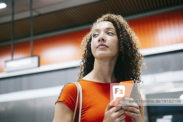 Young woman with mobile phone standing at subway station