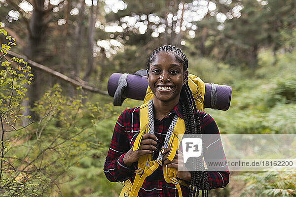 Glückliche junge Frau mit Rucksack steht im Wald