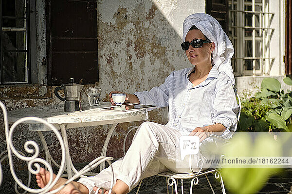 Reife Frau mit Sonnenbrille beim Kaffee auf der Terrasse