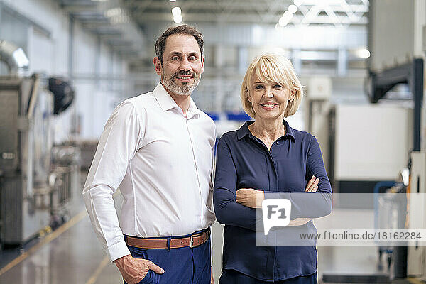 Happy senior businesswoman with arms crossed standing by colleague in industry