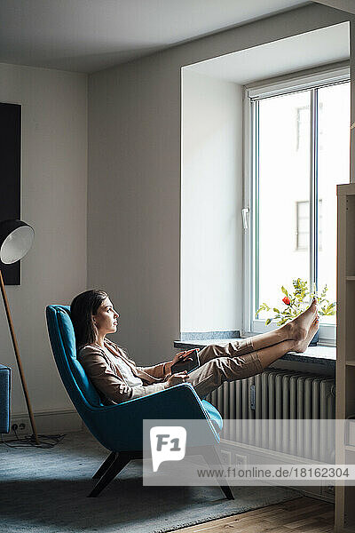 Thoughtful businesswoman sitting on chair with feet up at home