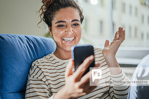 Happy woman gesturing on talking video call through smart phone at home