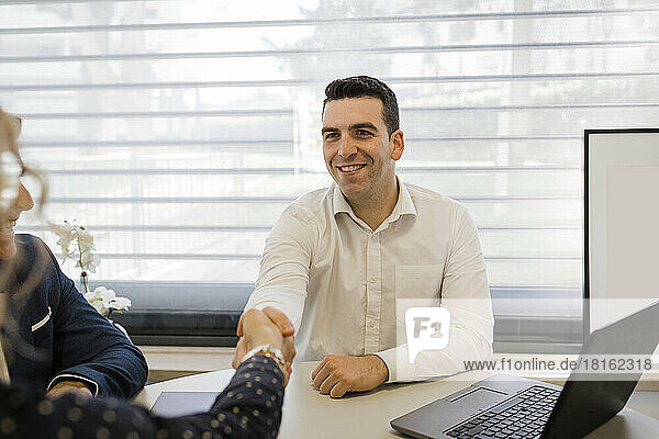 Happy businessman shaking hands with colleague at desk in office