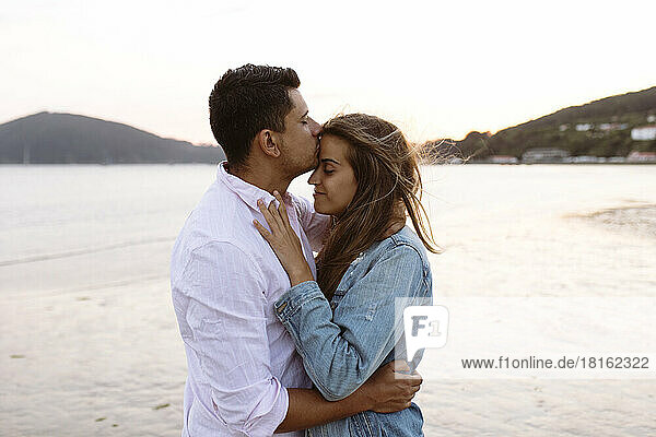 Junger Mann küsst Freundin am Strand auf die Stirn