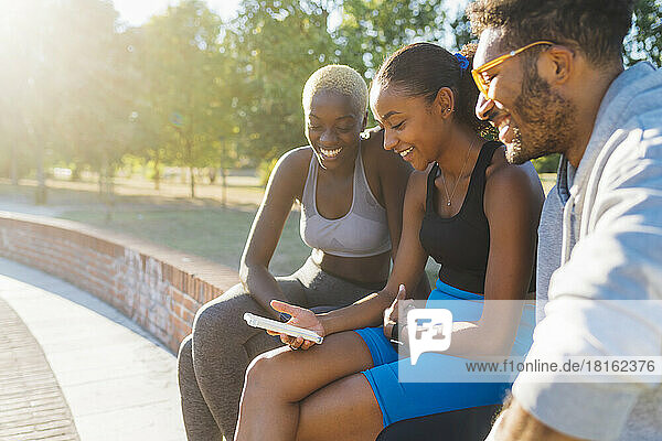Smiling sportswoman sharing mobile phone with friends