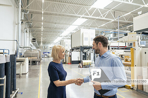 Smiling senior businesswoman shaking hand with colleague in industry