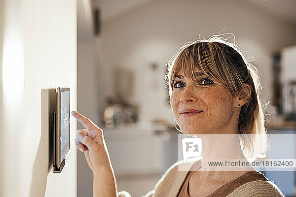 Smiling woman using smart home app on tablet at home