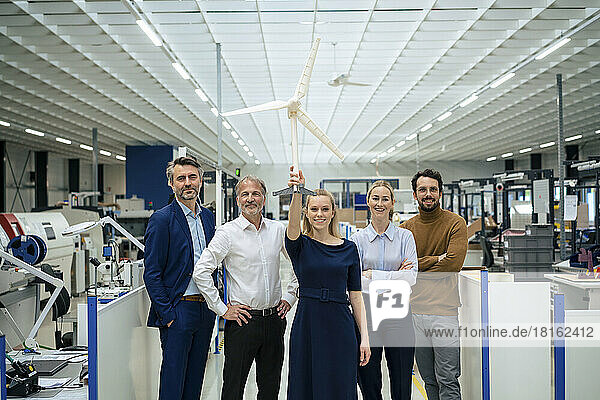 Happy young businesswoman holding wind turbine model standing with colleagues at industry