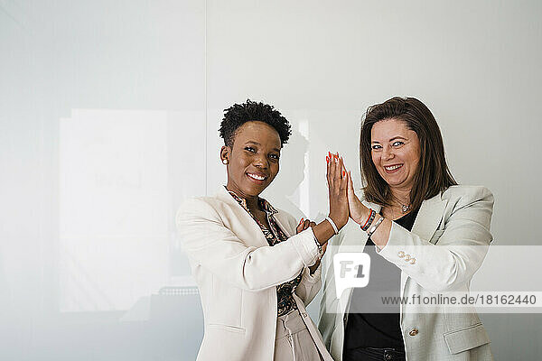 Happy business colleagues giving high-five to each other in front of white wall