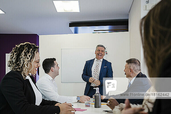 Happy mature businessman having meeting with colleagues sitting at desk