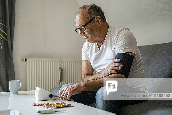 Älterer Mann benutzt Blutdruckmessgerät und sitzt zu Hause auf dem Sofa