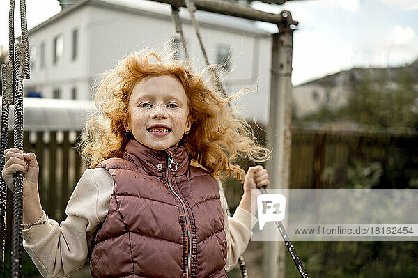 Smiling redhead girl swinging in garden