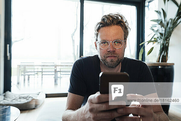 Mature man wearing eyeglasses holding smart phone at home