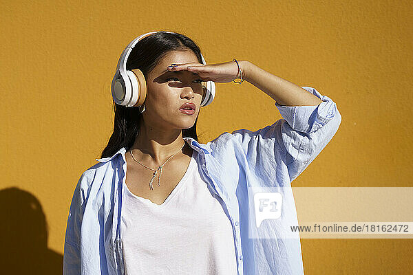 Woman wearing headphones shielding eyes in front of wall