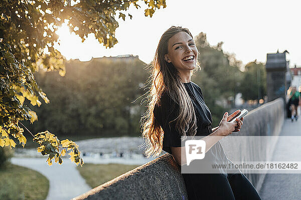 Cheerful woman with smart phone leaning on wall