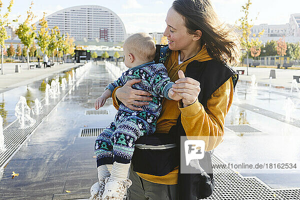 Mother playing with son at urban park by fountains