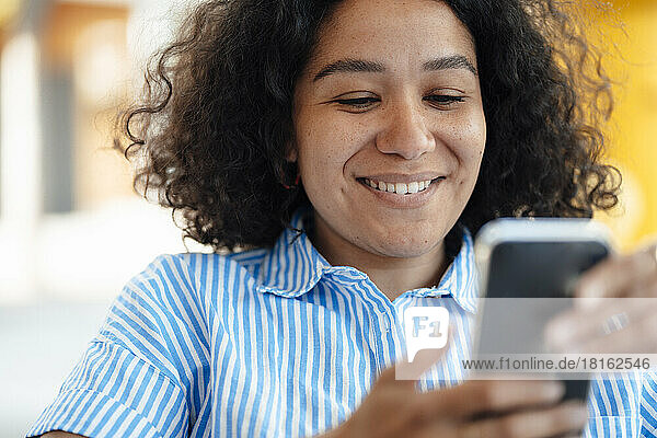 Smiling woman with curly hair using smart phone