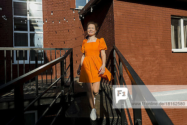 Smiling woman wearing orange dress moving down from staircase