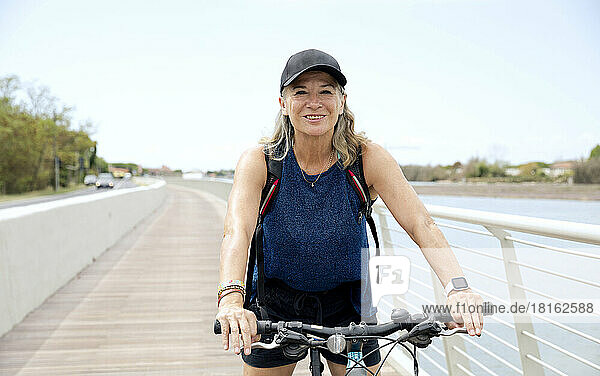 Happy senior woman wearing cap riding bicycle on promenade