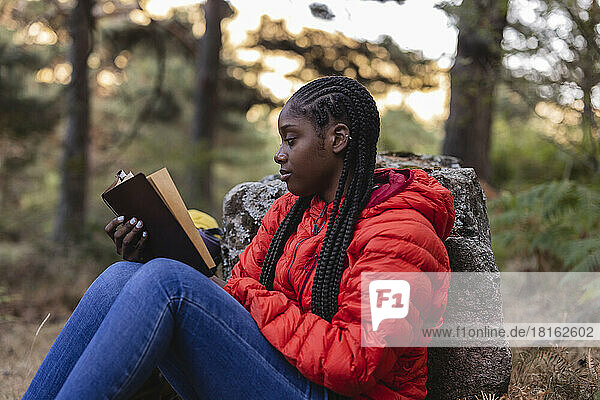 Young woman with braided hair reading book in forest